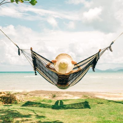 Summer vacations concept. Happy woman in black bikini relaxing in hammock on tropical beach